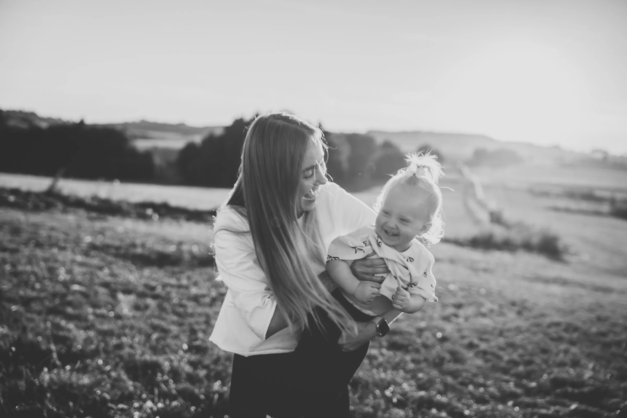 Maminka drží dceru v náručí na poli v podvečerním světle